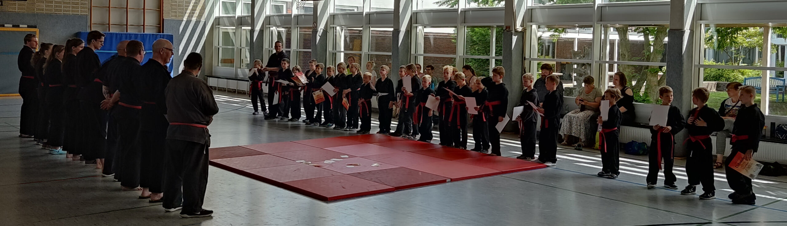 Kinder und Erwachsene in schwarzen Judoanzügen sich gegenüberstehend, Kinder haben Urkunden erhalten