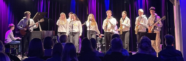 Band in weißen Pullovern mit Instrumenten auf Bühne