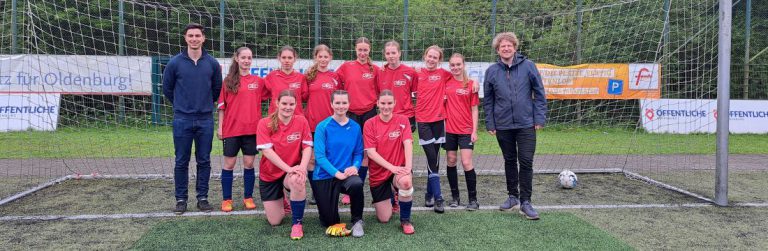 Fußballspielerinnen mit Lehrer im Tor posierend