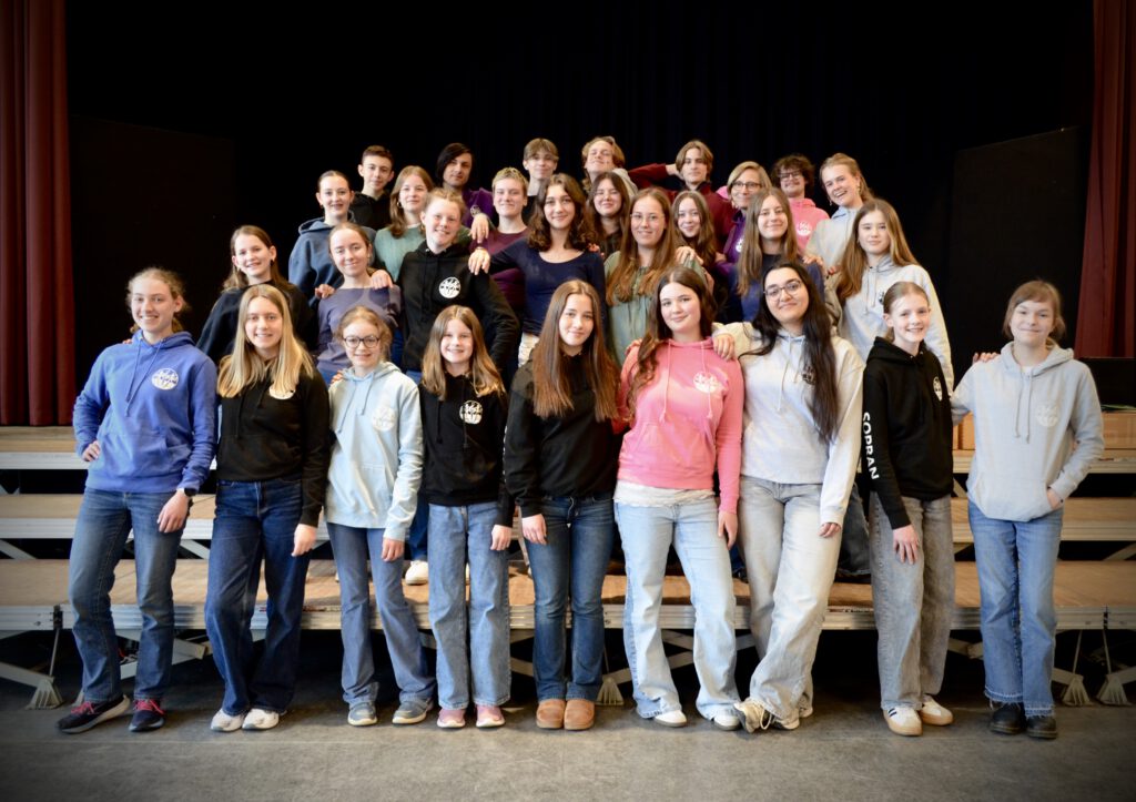 zahlreiche Schülerinnen und Schüler mit Schulpullover auf Bühne posierend