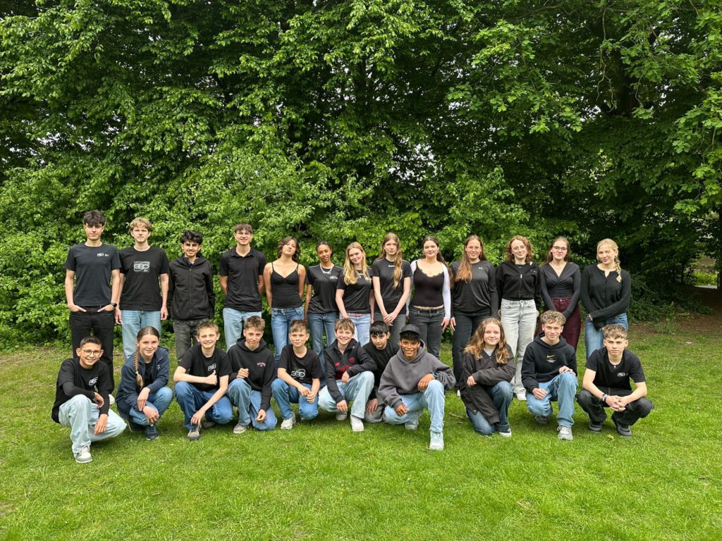 24 Schülerinnen und Schüler mit schwarzen Schul T-shirts im Grünen - die Schülervertretung