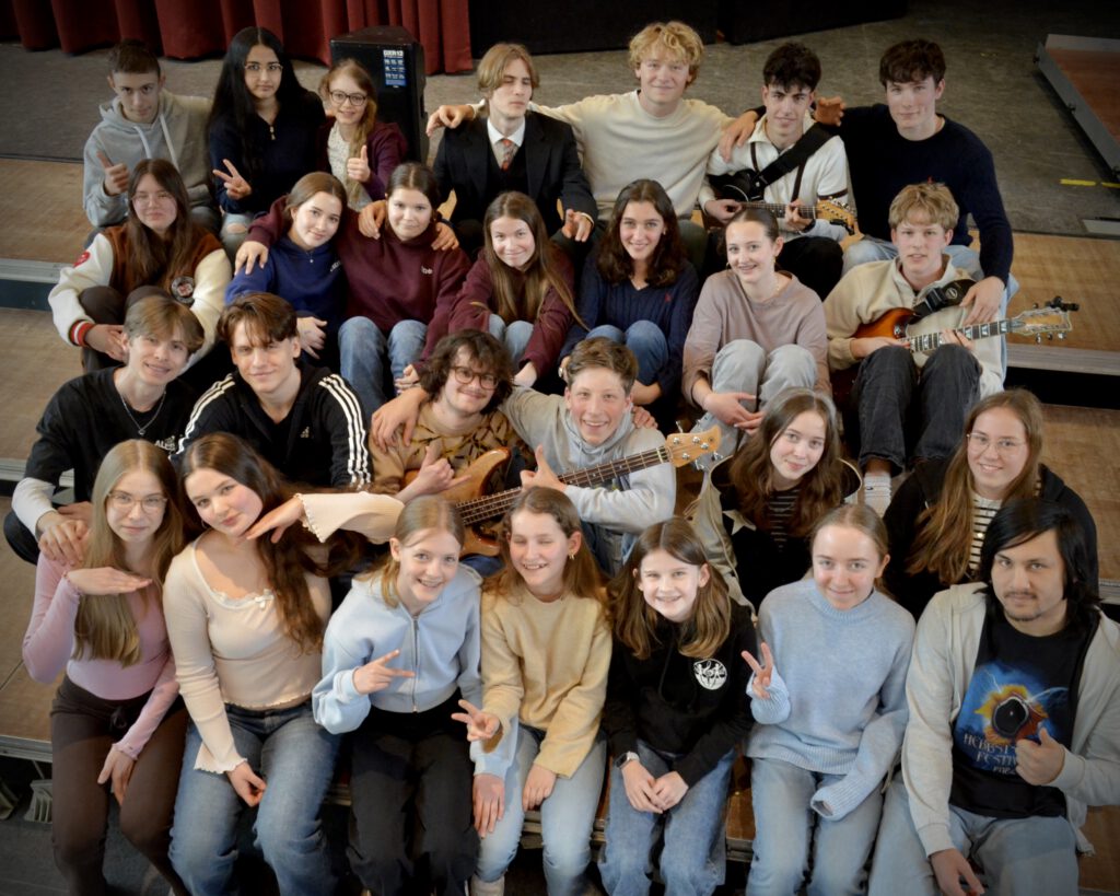 viele Schülerinnen und Schüler z. T. mit Gitarre posierend auf Bühne
