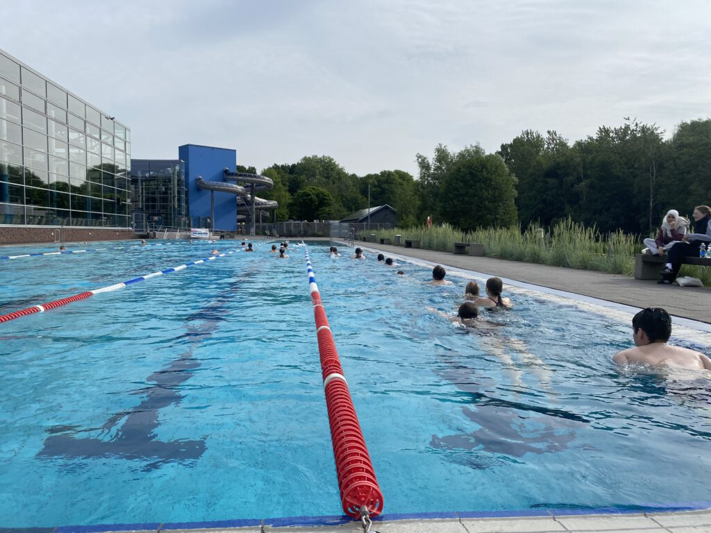 Schüler im Schwimmband ihre Bahnen ziehend von hinten