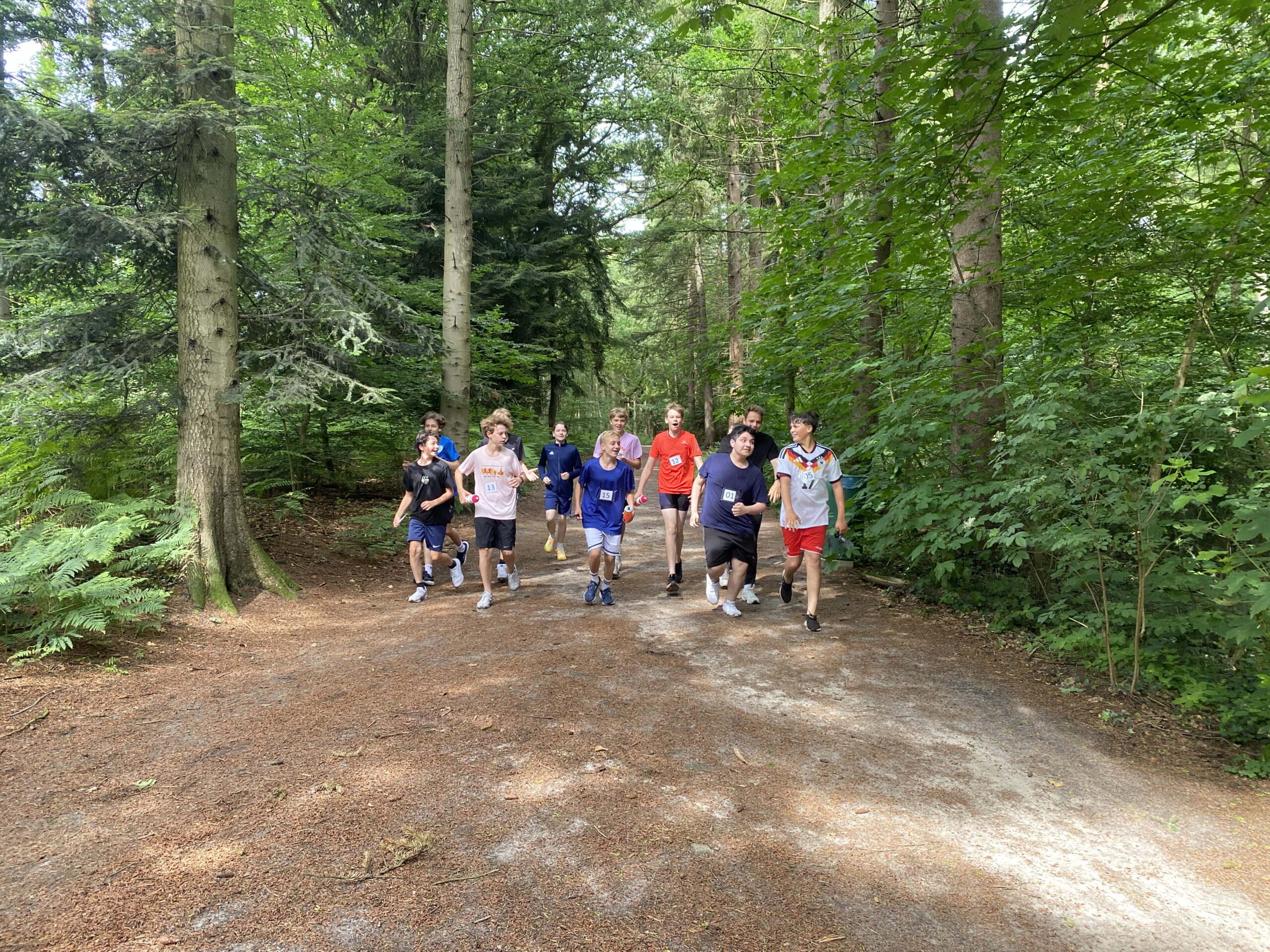 11 Schüler die fröhlich durch einen Wald laufen